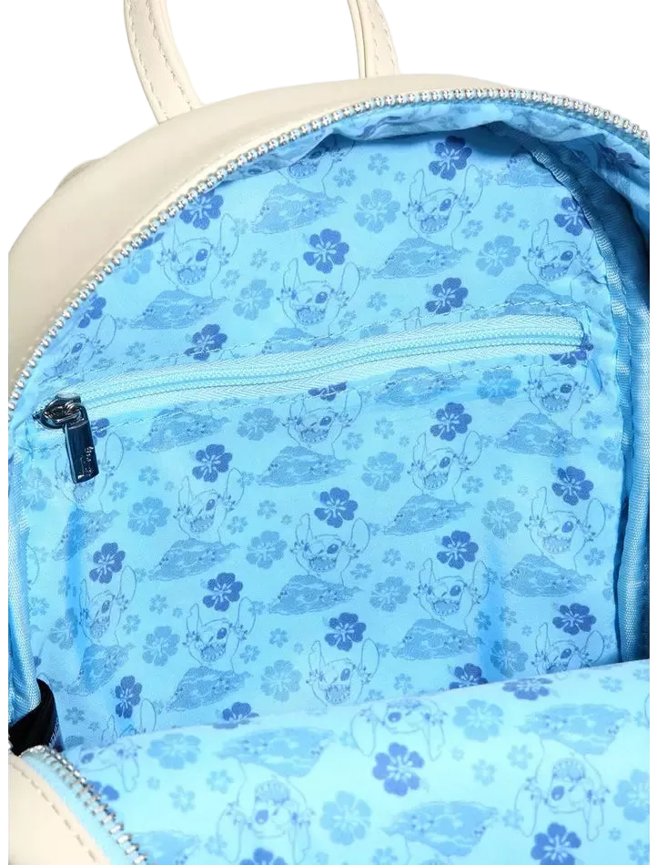 Close-up of the inside of a cream-colored backpack, showing a light blue patterned lining with cartoon characters and flowers, a zippered pocket, and silver zippers.