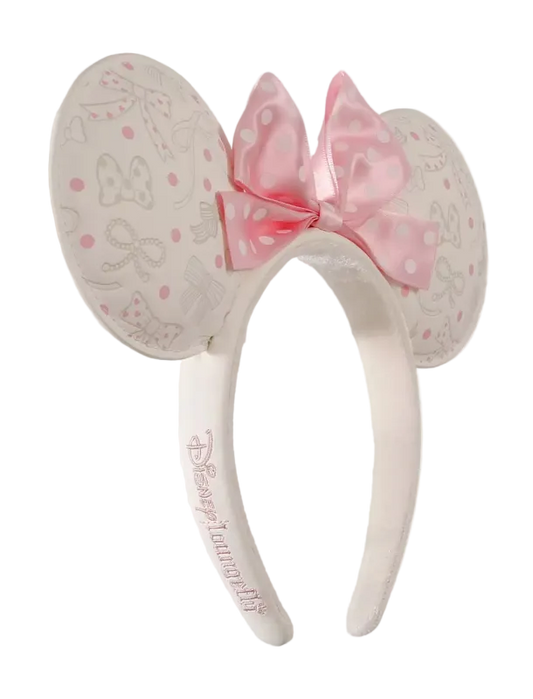A pair of Minnie Mouse-themed mouse ears headband featuring a pink polka-dot bow and embossed Minnie Mouse designs on a light cream background, with 'Disneyanna Fly' embroidered on the band.