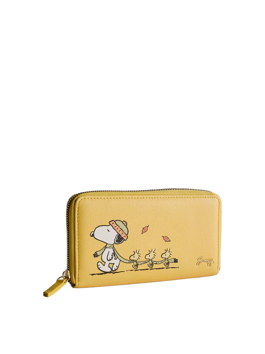 A yellow zip-around wallet featuring a printed cartoon illustration of Snoopy and the Beagle dogs walking under falling leaves, shown on a light gray background.