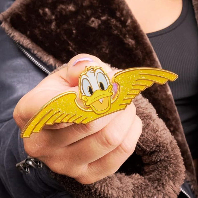 Hand holding a yellow cartoon character pin with a brown jacket background