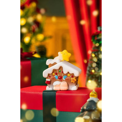 Decorative gingerbread house figurine on a red and green box with Christmas tree and lights in the background.