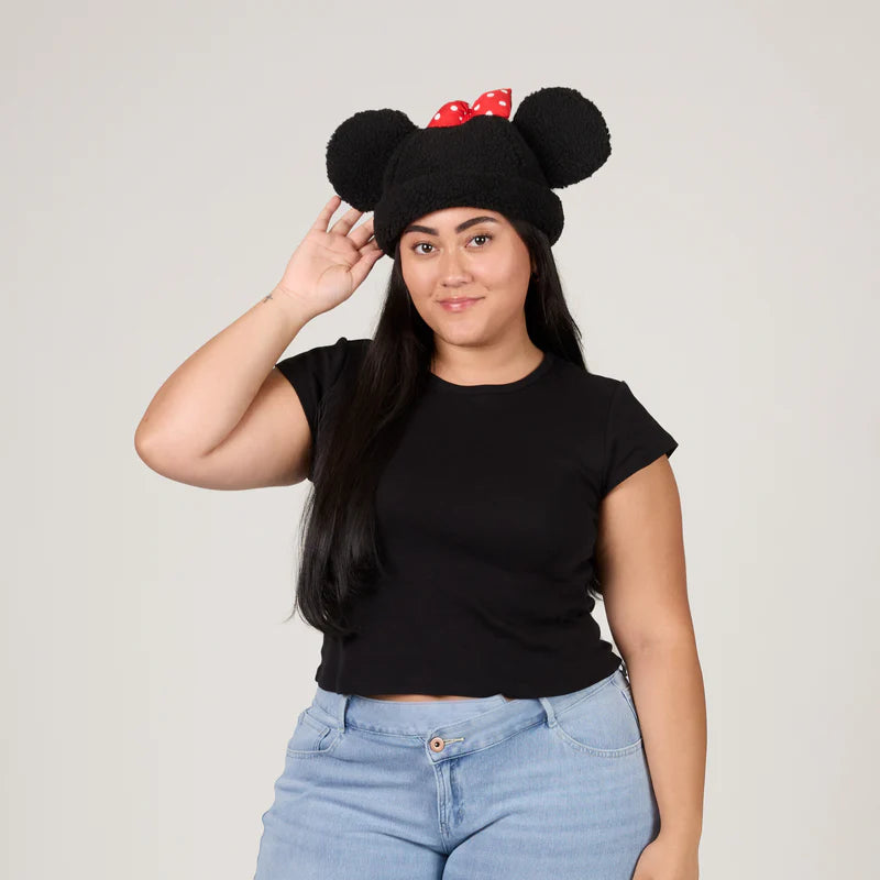 Person wearing a black hat with large ears and red bow, standing against a plain background
