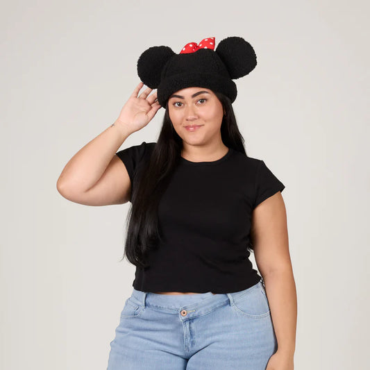 Person wearing a black hat with large ears and red bow, standing against a plain background