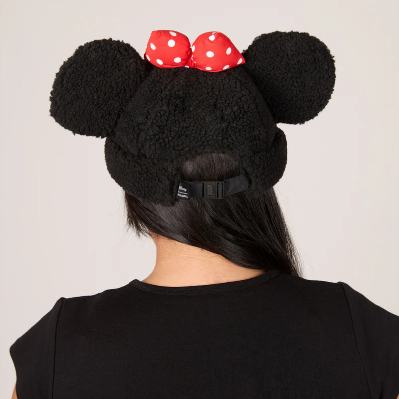 Black fleece beanie with large ears and a red polka dot bow on a plain background