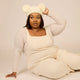Woman wearing a cream-colored outfit with a matching hat on a plain background