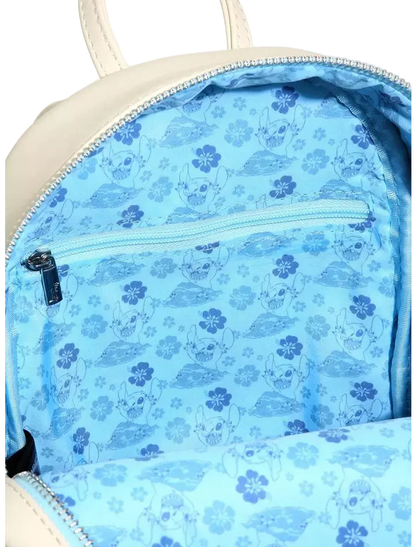 Close-up of the inside of a cream-colored backpack, showing a light blue patterned lining with cartoon characters and flowers, a zippered pocket, and silver zippers.
