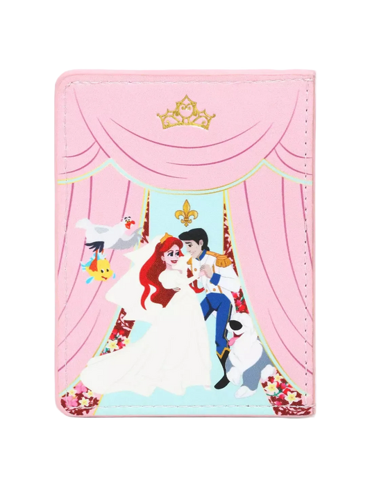 A pink faux leather passport cover featuring a graphic of Disney's The Little Mermaid and Ariel on a stage-like backdrop with pink curtains, a gold tiara, and small character illustrations.