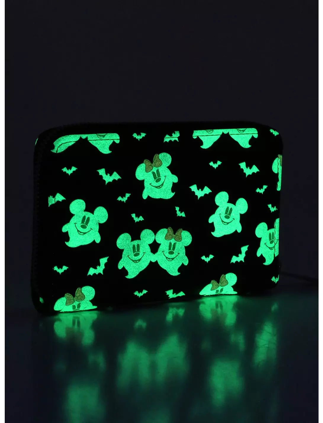 A black zip-around wallet with a glowing green Halloween pattern of Mickey Mouse silhouettes, ghosts, and bats, shown on a dark reflective surface.