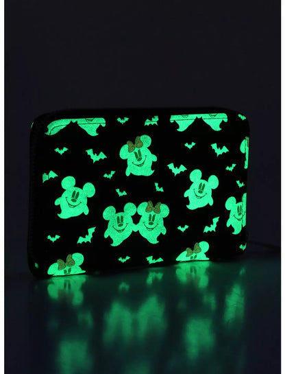 A black zip-around wallet with a glowing green Halloween pattern of Mickey Mouse silhouettes, ghosts, and bats, shown on a dark reflective surface.