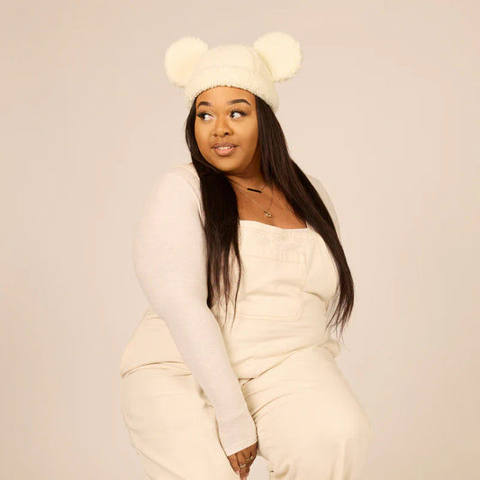 Woman wearing a cream-colored outfit with a matching hat on a plain background