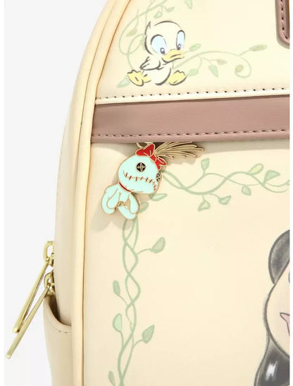 Close-up of a cream-colored backpack featuring Disney's Tropezana character artwork, a mauve horizontal trim, and a decorative enamel pin of a blue bird with a red bow.