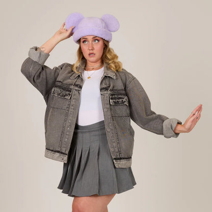 Person wearing a gray jacket, white shirt, and gray pleated skirt with a purple fluffy hat.