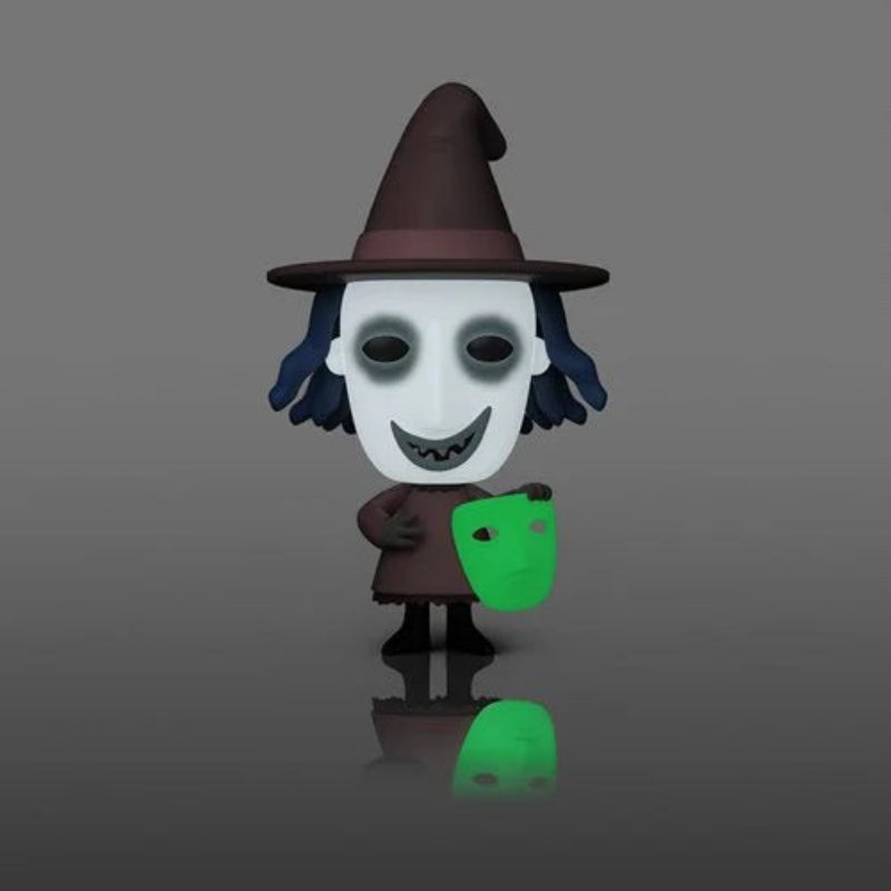 A stylized cartoon figure of a witch holding a glowing green mask, standing on a dark gray reflective surface against a gray gradient background.
