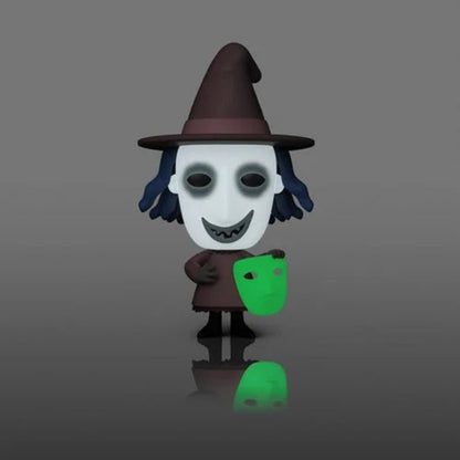 A stylized cartoon figure of a witch holding a glowing green mask, standing on a dark gray reflective surface against a gray gradient background.