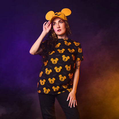 Person wearing a black t-shirt with yellow mouse head patterns and a matching cap against a purple and orange gradient background.