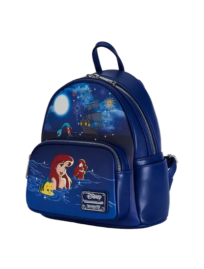 A blue faux-leather Disney/Loungefly mini backpack featuring characters from The Little Mermaid, including Ariel, Sebastian, and Flounder, with a navy night-sky print on the upper half and a front pocket with character graphics.