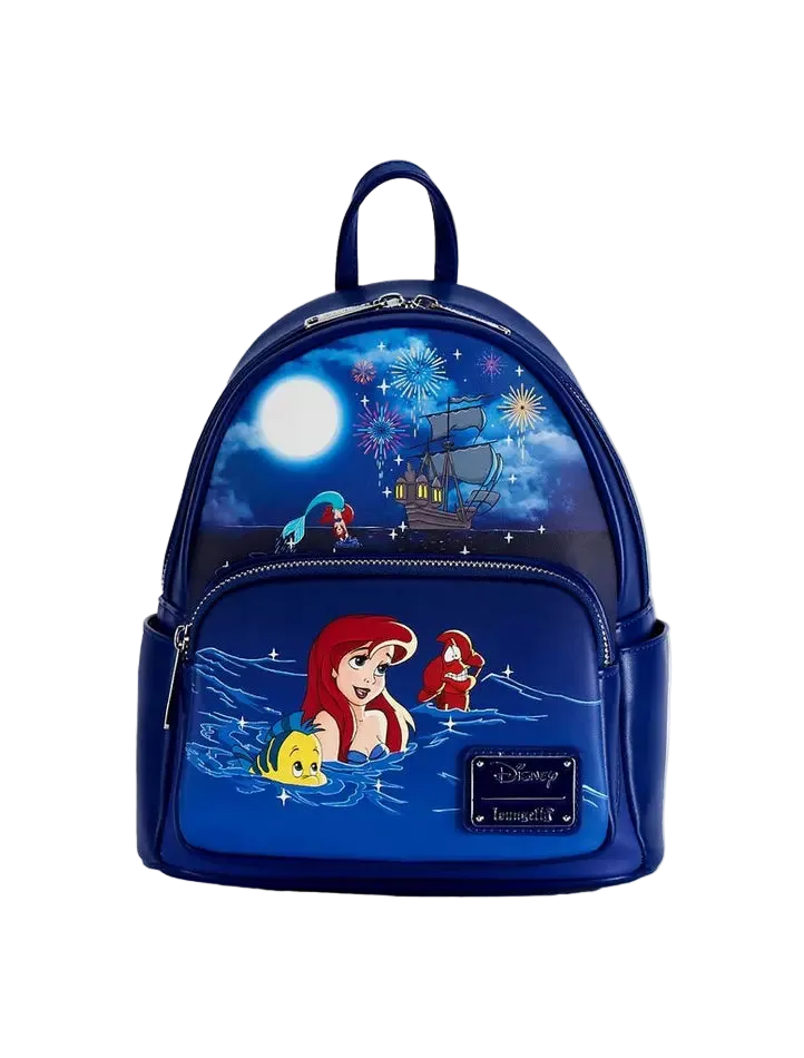 A Disney The Little Mermaid mini backpack in navy blue, featuring character artwork of Ariel, Sebastian, and Flounder under a starry night sky with fireworks and a ship, on a light gray background.