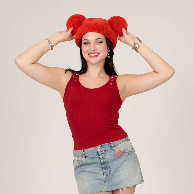 Woman wearing a red knit hat with bunny ears and a red tank top against a beige background