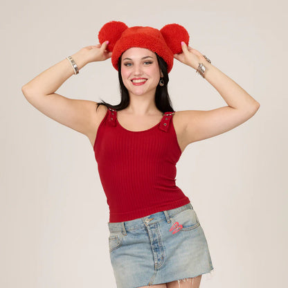 Woman wearing a red knit hat with bunny ears and a red tank top against a beige background