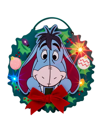 A festive Christmas wreath-shaped wall hanging featuring Eeyore from Winnie the Pooh, with a red bow at the bottom and glowing light effects around the wreath.