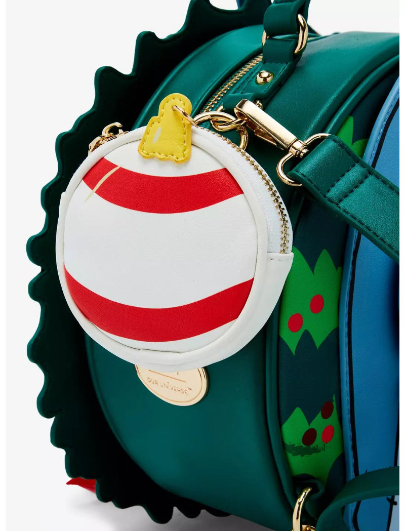 A close-up of a green round shoulder bag with a scalloped edge, featuring a white and red striped coin purse charm with a gold bell and a gold plaque, plus a blue side panel with green holly details.