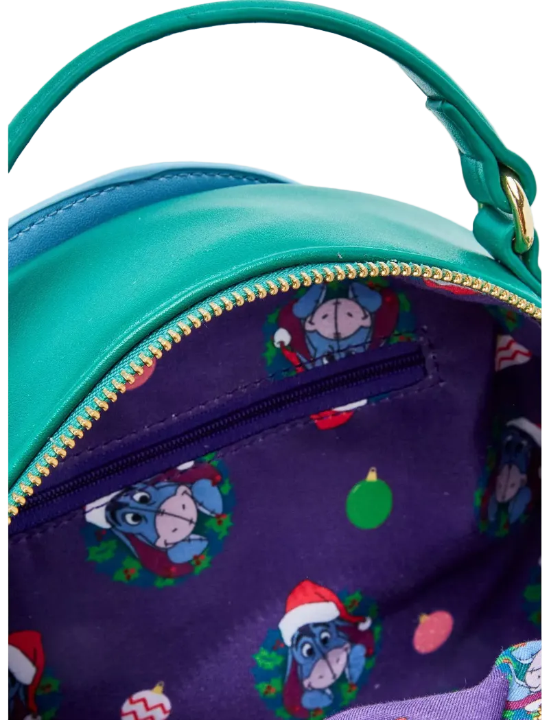 Close-up of a turquoise and purple handbag with a gold zipper. The interior is lined with a purple fabric featuring a repeating Easter egg-themed print of Eeyore wearing a Santa hat, surrounded by small holiday motifs.