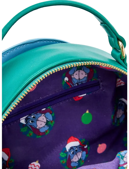 Close-up of a turquoise and purple handbag with a gold zipper. The interior is lined with a purple fabric featuring a repeating Easter egg-themed print of Eeyore wearing a Santa hat, surrounded by small holiday motifs.