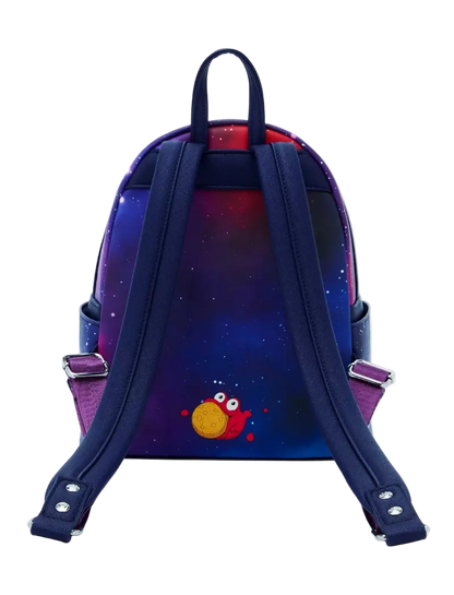 A small backpack shown from the back, featuring a dark blue and purple galaxy print with a small red and yellow cartoon character near the bottom. The backpack has thick navy blue shoulder straps and silver metal buckles on the side straps.