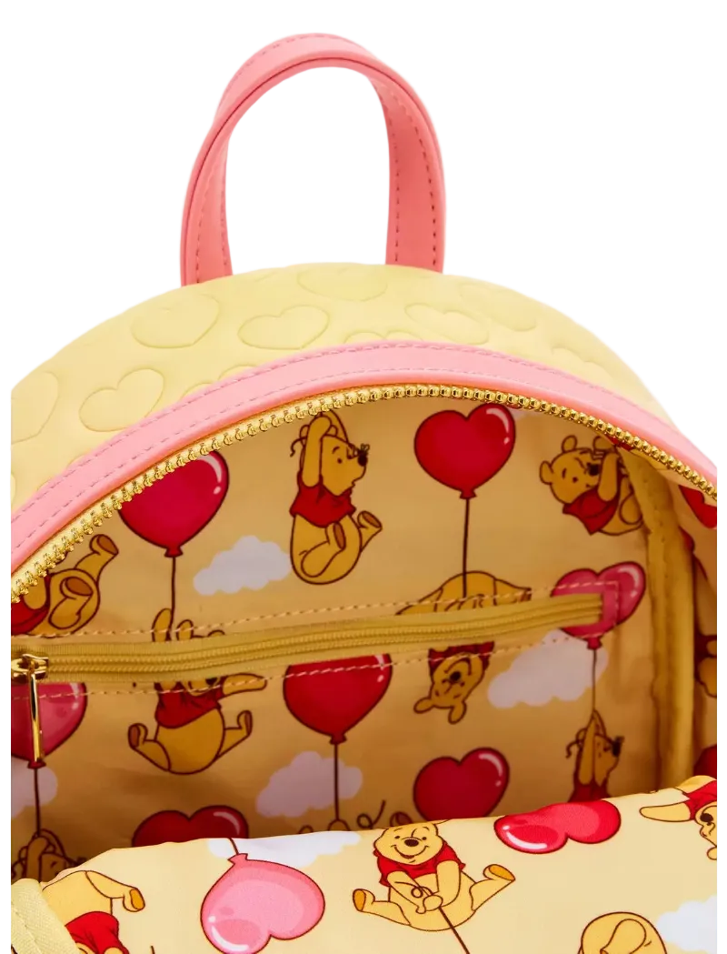 Close-up of a Winnie the Pooh backpack with a yellow body, pink handles and trim, and a heart-and-pooh print lining the interior.