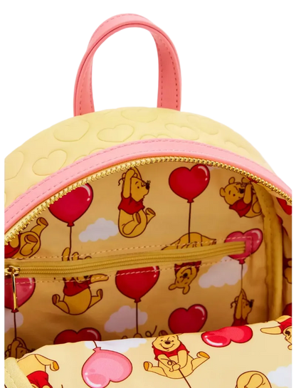 Close-up of a Winnie the Pooh backpack with a yellow body, pink handles and trim, and a heart-and-pooh print lining the interior.