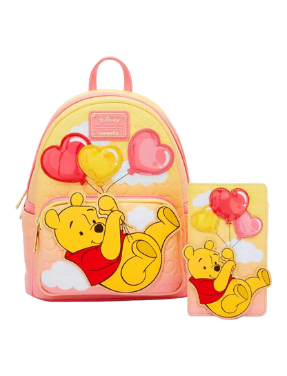 A pink and yellow Disney Winnie the Pooh backpack set shown with a matching zip-around wallet. The set features a 3D applique of Winnie the Pooh lying on clouds and holding pink and yellow heart balloons, with a pink quilted background and a pink top handle.