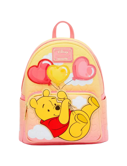 A pastel pink and yellow Disney Winnie the Pooh backpack featuring a large applique of Winnie the Pooh holding red and yellow heart-shaped balloons, with a pink Disney Memory Lane patch on the front.