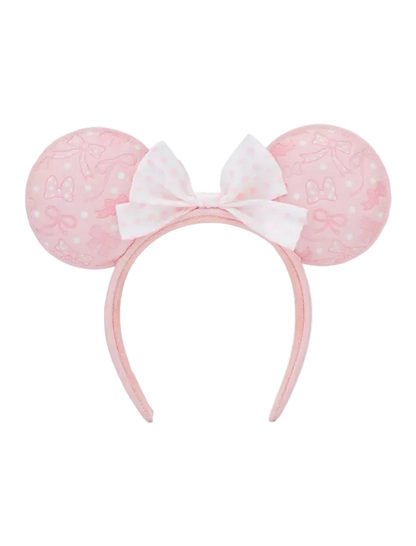 A pink and white Minnie Mouse-themed headband with round ears featuring a subtle bow pattern and a central white bow with pink polka dots, shown against a plain white background.