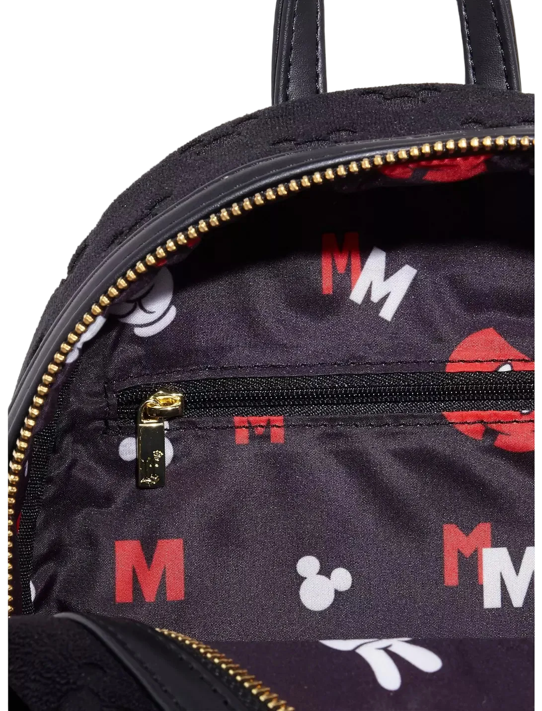 Close-up of a black backpack interior with gold zippers, a small zip pocket, and an allover Mickey Mouse-inspired print featuring red and white letters and silhouettes on a white background.