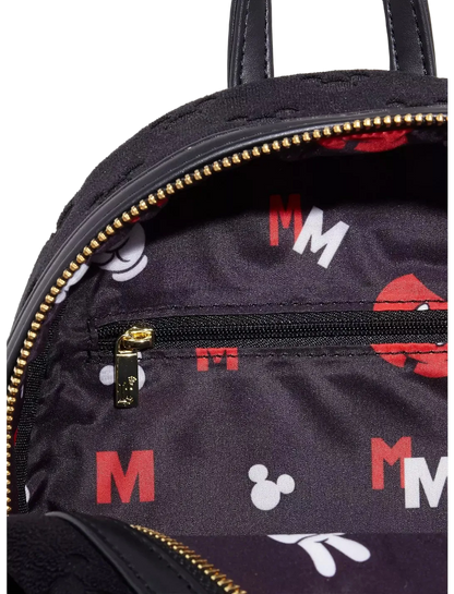 Close-up of a black backpack interior with gold zippers, a small zip pocket, and an allover Mickey Mouse-inspired print featuring red and white letters and silhouettes on a white background.