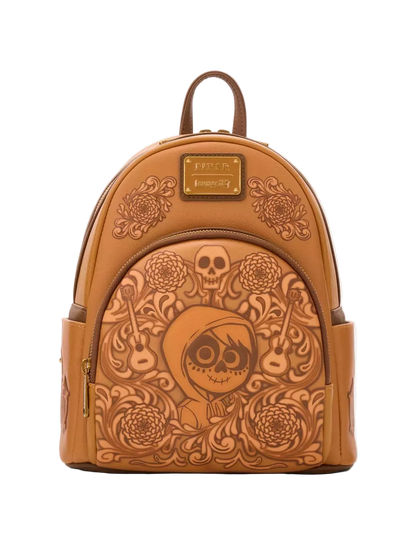 A tan leather mini backpack featuring an embossed Day of the Dead design with a central skeleton face, skulls, guitars, and floral patterns. The backpack has a top handle, zippered main compartment, side pockets, and a gold-tone metal brand plaque on the front.