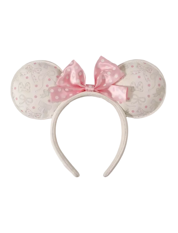 A Minnie Mouse-inspired headband with round ears covered in a light beige and pink Disney-themed pattern, featuring a large pink polka-dot bow on a white background.