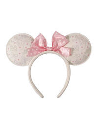 A Minnie Mouse-inspired headband with round ears covered in a light beige and pink Disney-themed pattern, featuring a large pink polka-dot bow on a white background.