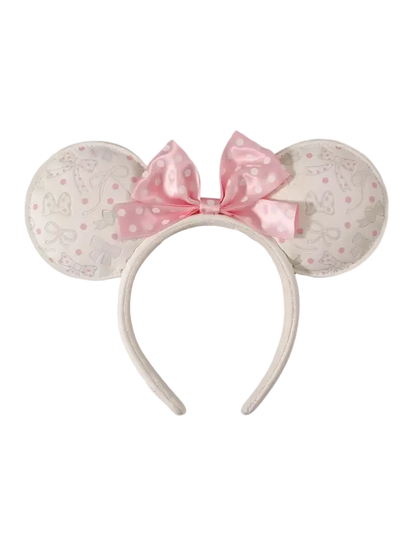 A Minnie Mouse-inspired headband with round ears covered in a light beige and pink Disney-themed pattern, featuring a large pink polka-dot bow on a white background.