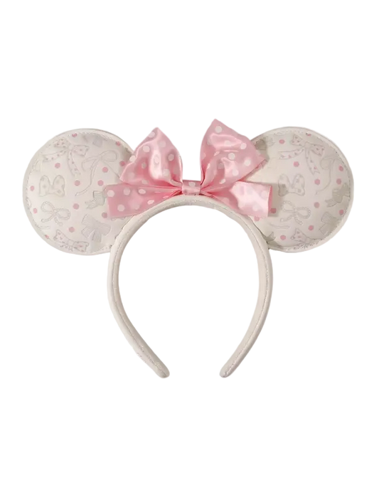 A Minnie Mouse-inspired headband with round ears covered in a light beige and pink Disney-themed pattern, featuring a large pink polka-dot bow on a white background.