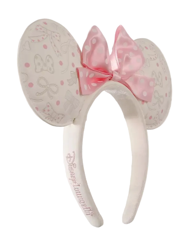 A pair of Minnie Mouse-themed mouse ears headband featuring a pink polka-dot bow and embossed Minnie Mouse designs on a light cream background, with 'Disneyanna Fly' embroidered on the band.