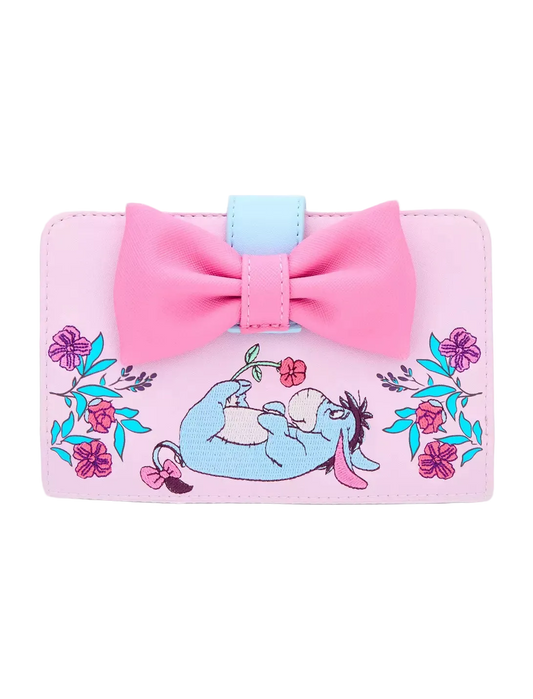 A pink wallet featuring a large pink bow on top, a light blue accent tab, and an embroidered illustration of Eeyore lying down surrounded by pink flowers and blue leaves, set against a plain white background.