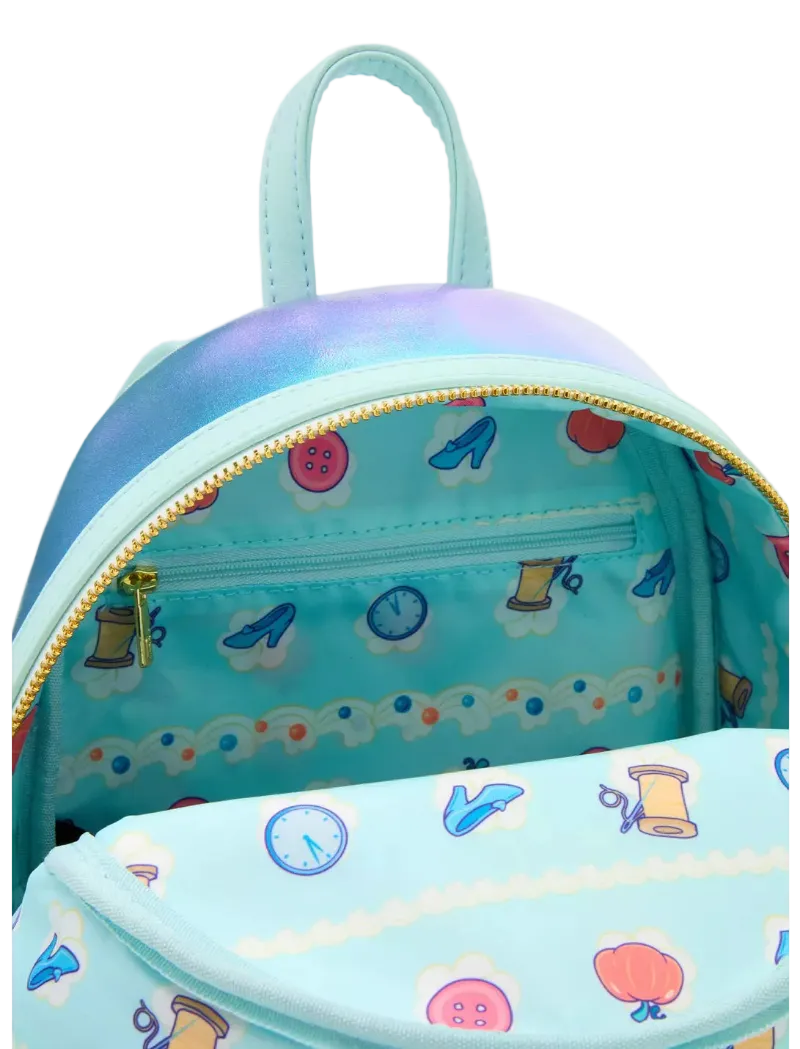 A light blue mini backpack with a colorful sewing-themed print inside and on the front pocket, featuring a gold zipper and a matching top handle.
