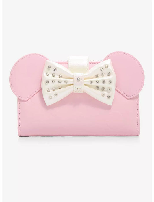 A pink faux-leather clutch bag featuring Minnie Mouse-inspired round ears and a large white bow embellished with rhinestones, shown against a plain white background.