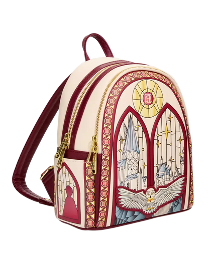 A small backpack with a cream and burgundy design inspired by stained glass, featuring gold zippers and a printed illustration of a cathedral, a dove, and a silhouette.