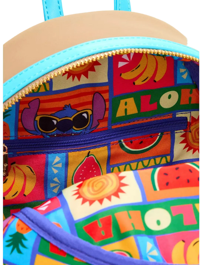Close-up of a colorful backpack interior with a tropical Aloha patchwork print featuring cartoon characters, fruits, and text, with a turquoise zipper and a beige exterior visible at the top.