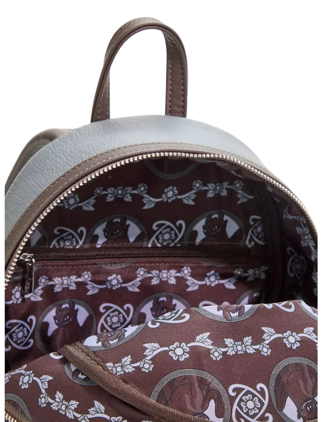 Close-up of the interior of a small backpack with a light gray exterior and a brown patterned lining featuring white floral and circular motifs.