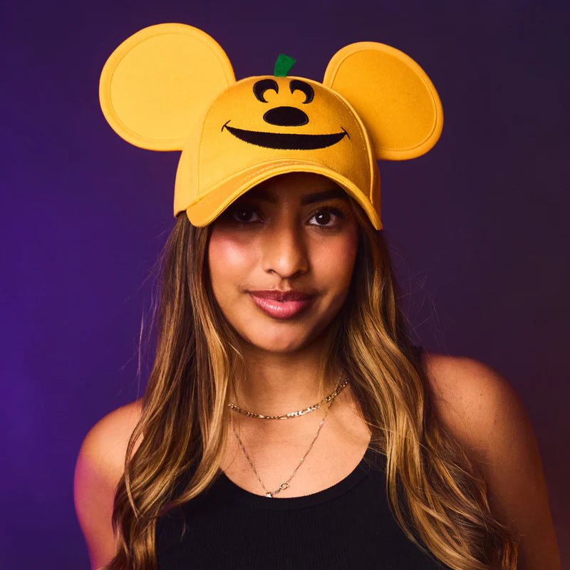 Person wearing a yellow cap with mouse ears and a smiley face design on a purple background