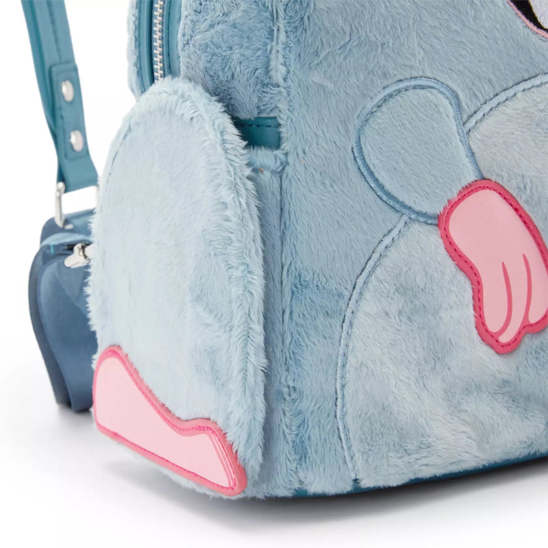 Close-up of a plush light blue bunny backpack with pink applique ears and a teal shoulder strap on a white background.