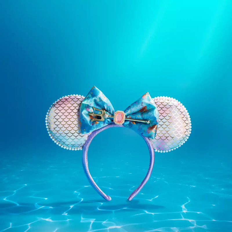 Mermaid-themed mouse ears headband with a blue patterned bow, mermaid scale patterned ears, and a purple headband, set against an underwater pool background.
